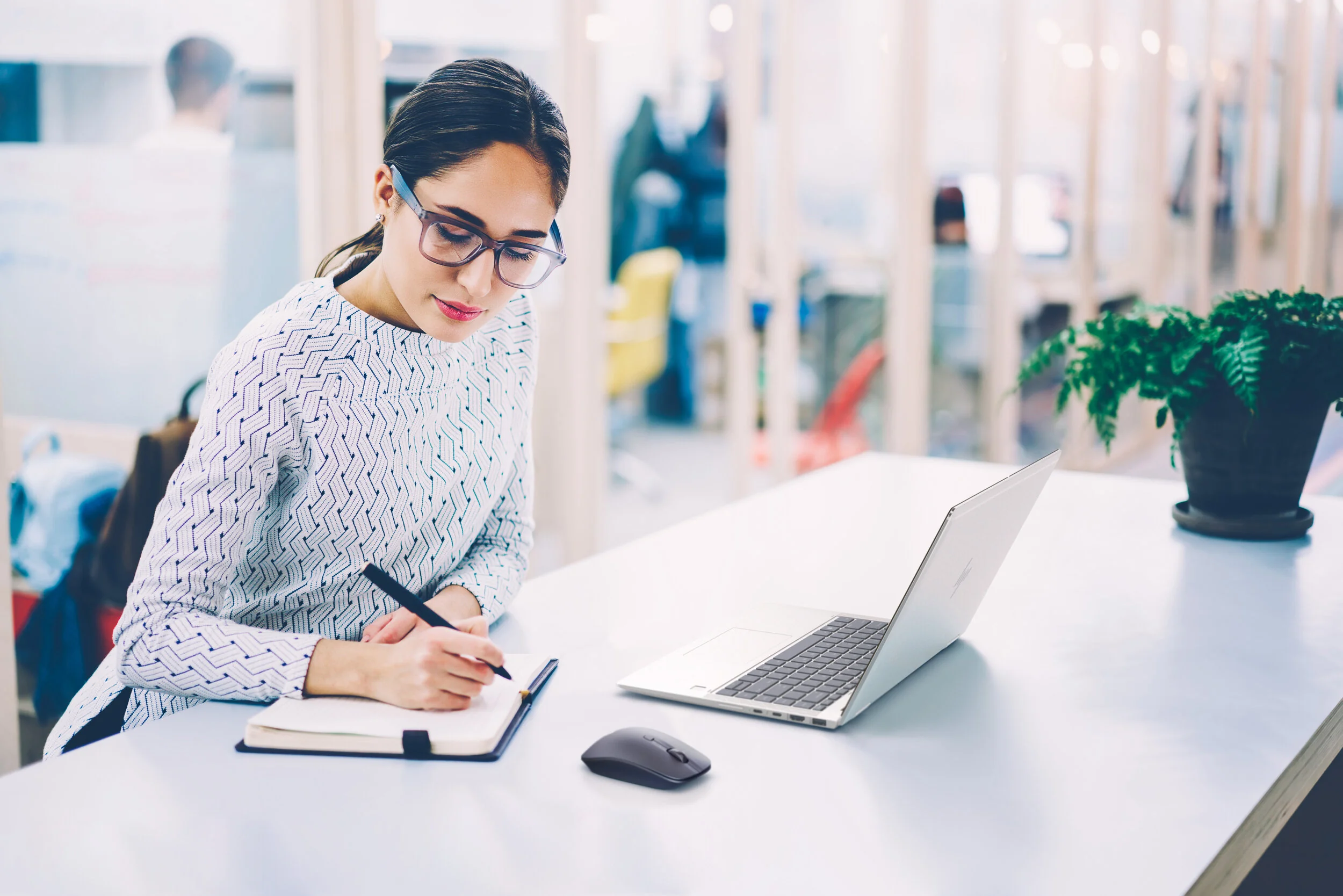 Woman writing in a notebook beside a silver laptop